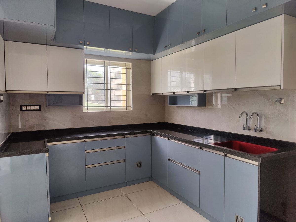 L-shaped modular kitchen with blue-grey base cabinets, white wall cabinets and a black granite counter