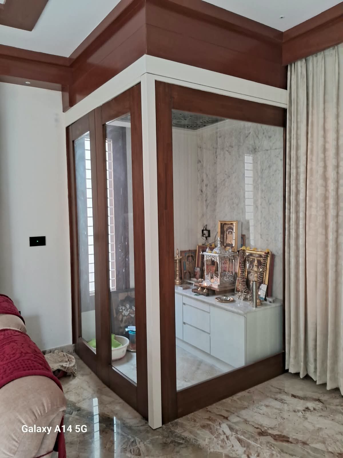 Pooja room enclosed in glass with a wood-finish frame and white storage cabinet